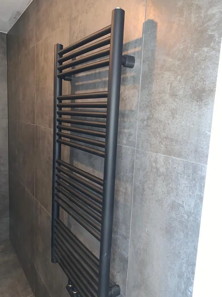 Zwarte handdoekradiator tegen grijze tegels (projectfoto bij review van Partoredjo)